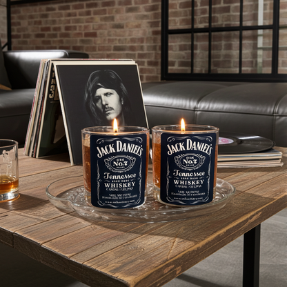 Two Jack Daniel's whiskey candles on a wooden table with a brick wall background.