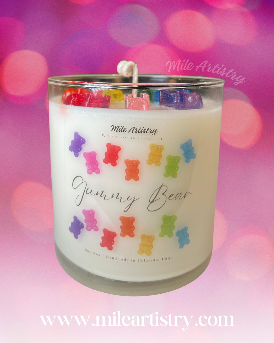 Candle with colorful gummy bear design and 'Mile Artistry' branding on a blurred pink and purple background.