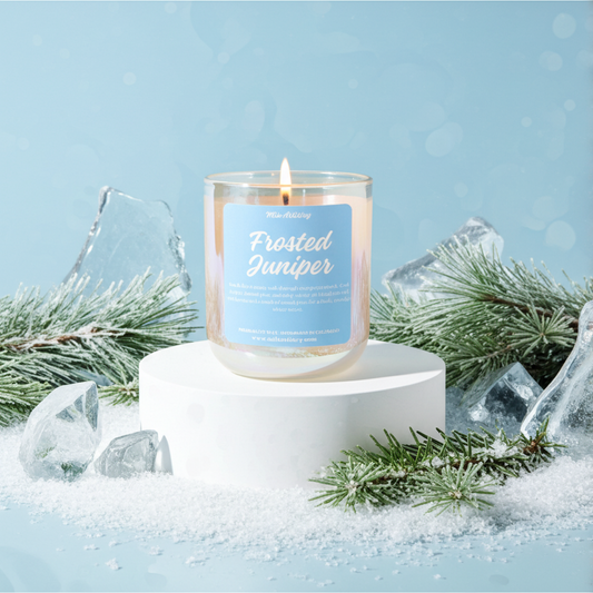 Candle labeled 'Frosted Juniper' with winter-themed decorations on a light blue background