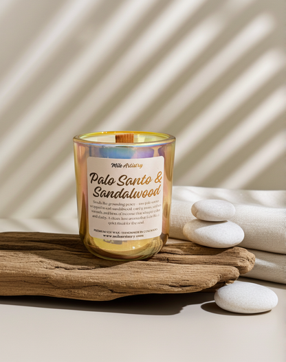 Candle labeled 'Palo Santo & Sandalwood' on a wooden surface with stones and a neutral background