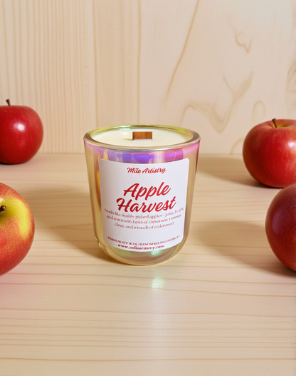 Candle labeled 'Apple Harvest' surrounded by red apples on a wooden surface
