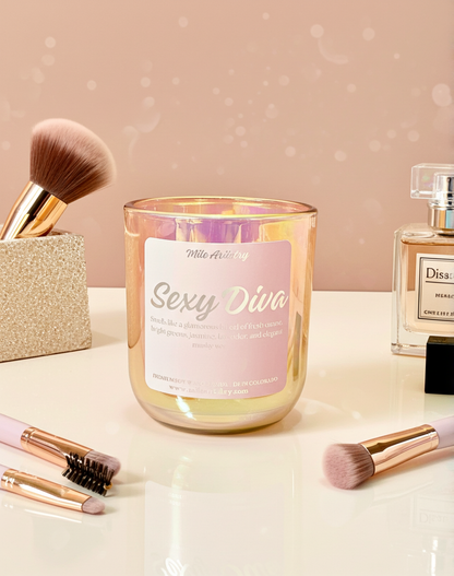 Candle labeled 'Sexy Diva' with makeup brushes and perfume on a reflective surface.